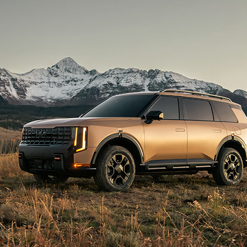 A side view of the 2027 Kia Telluride X-Pro in brown parked in a grassy field with snowy mountains in the background.