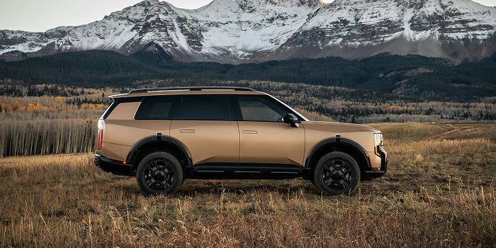 Side view of the 2027 Kia Telluride X-Pro in matte brown parked in a grassy field with snow-capped mountains in the background.