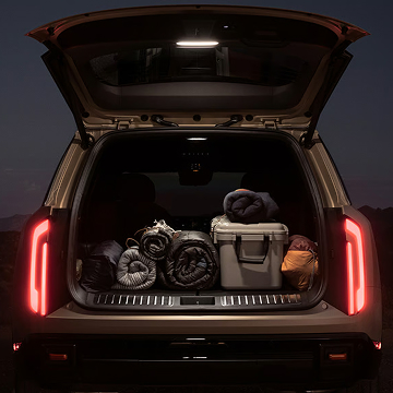 Photo of the 2027 Kia Telluride with an open trunk showcasing the spacious cargo area packed with outdoor gear, illuminated taillights, and liftgate lamp, set against a hillside backdrop.