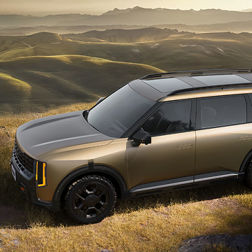 2027 Kia Telluride X-Pro SX Prestige in brown with black accents, featuring bold vertical LED headlights, black alloy wheels, and roof rails, parked on a grassy hilltop with panoramic lush mountain views.